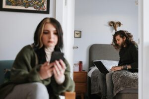 Ett par som sitter med en telefon och dator separat. Kvinnan ger en känsla av att känna sig ensam i en relation.
